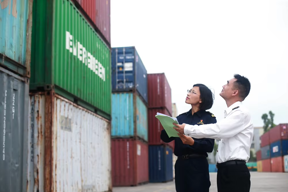 Staff checking documents beside shipping containers